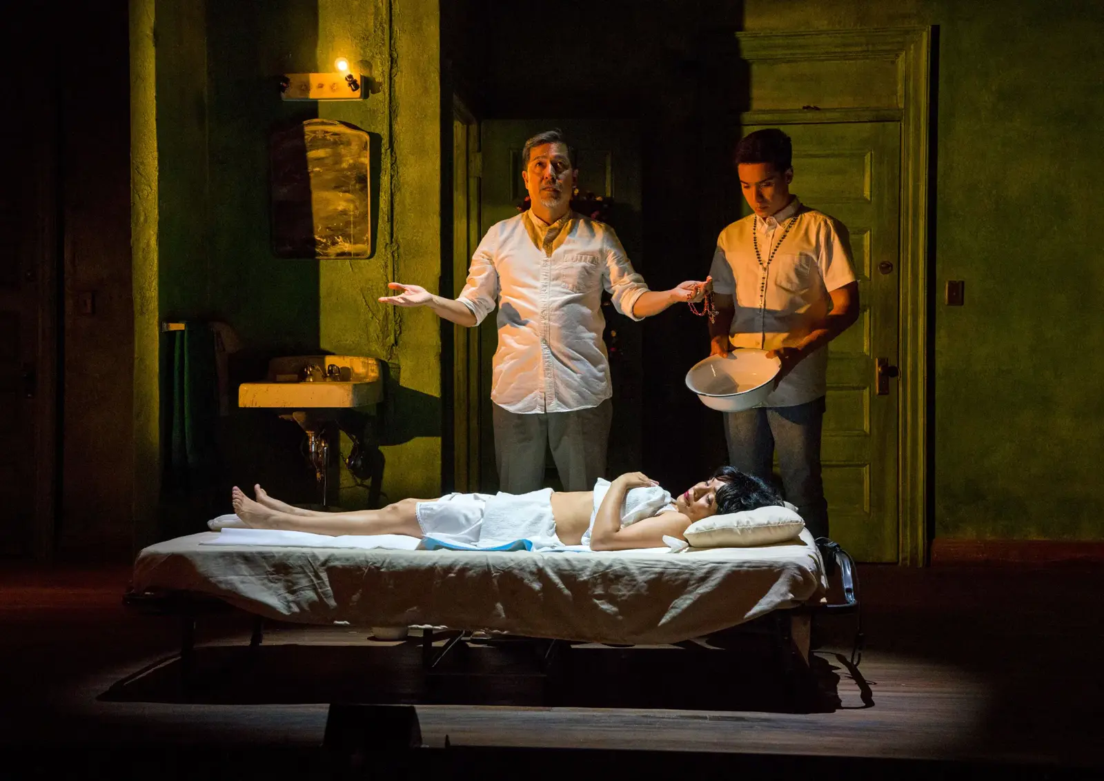 Dimly lit theater scene of a family at a bedside